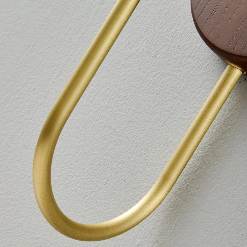 La base in legno arrotondata conferisce all'apparecchio un aspetto morbido, simile a quello di un mobile, mentre il braccio metallico curvo mantiene il paralume sollevato ed equilibrato.