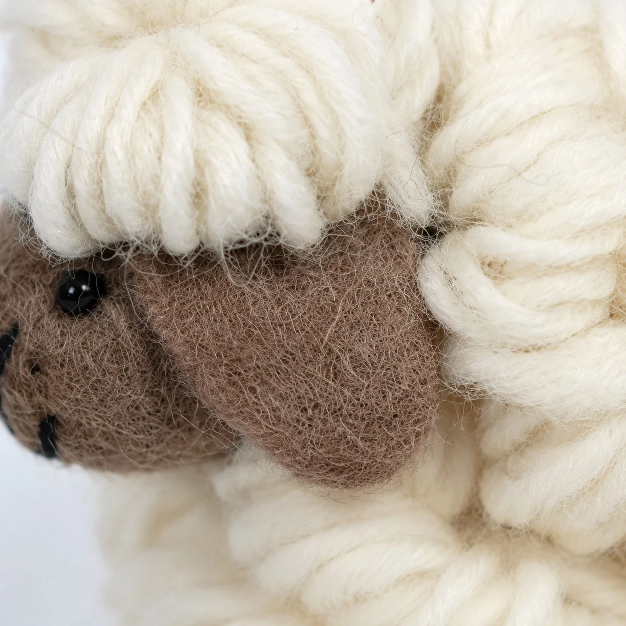 Detailweergave van een bruin vilten schapengezicht en crèmekleurige wollen vacht
