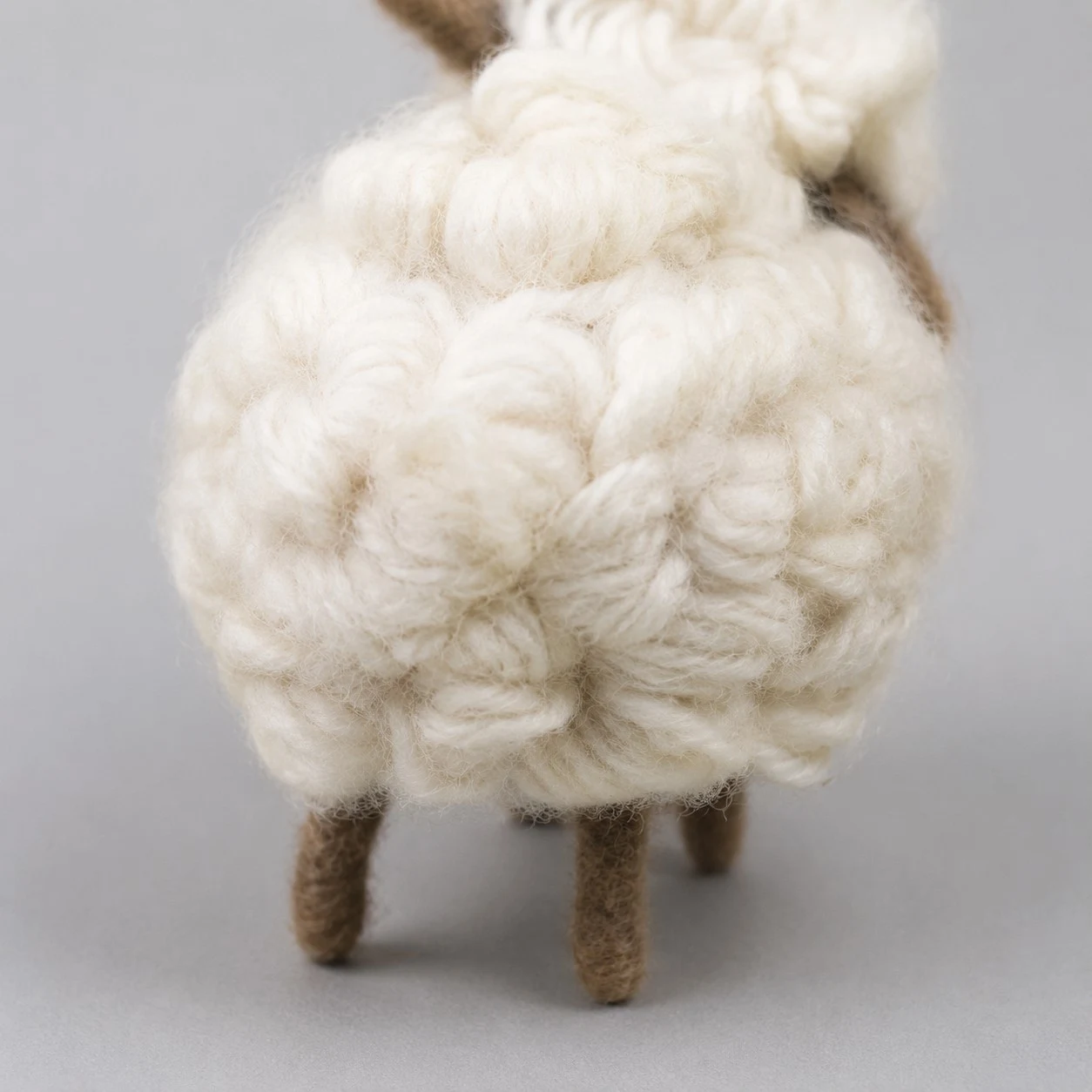 gekrulde crèmekleurige wollen fleece met een bruin vilten gezichtsdetail.