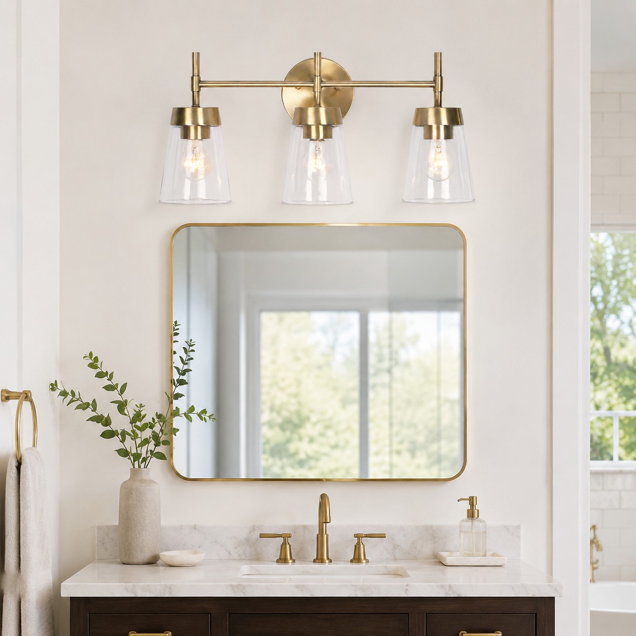 Lampadario a tre luci in ottone spazzolato installato sopra lo specchio del bagno.